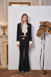 Woman in a black outfit standing next to a wooden horse model in an elegant interior setting.