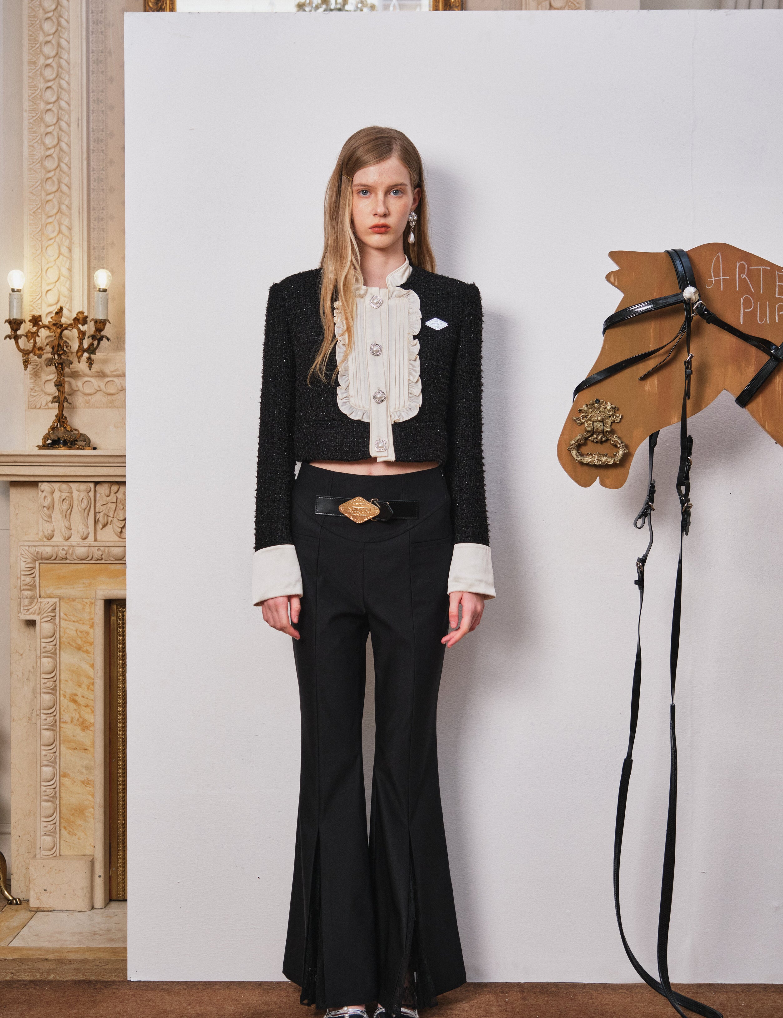 Woman in a black outfit standing next to a wooden horse model in an elegant interior setting.