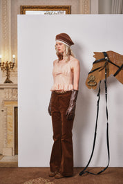 Person in vintage clothing standing next to a horse head sculpture with bridle